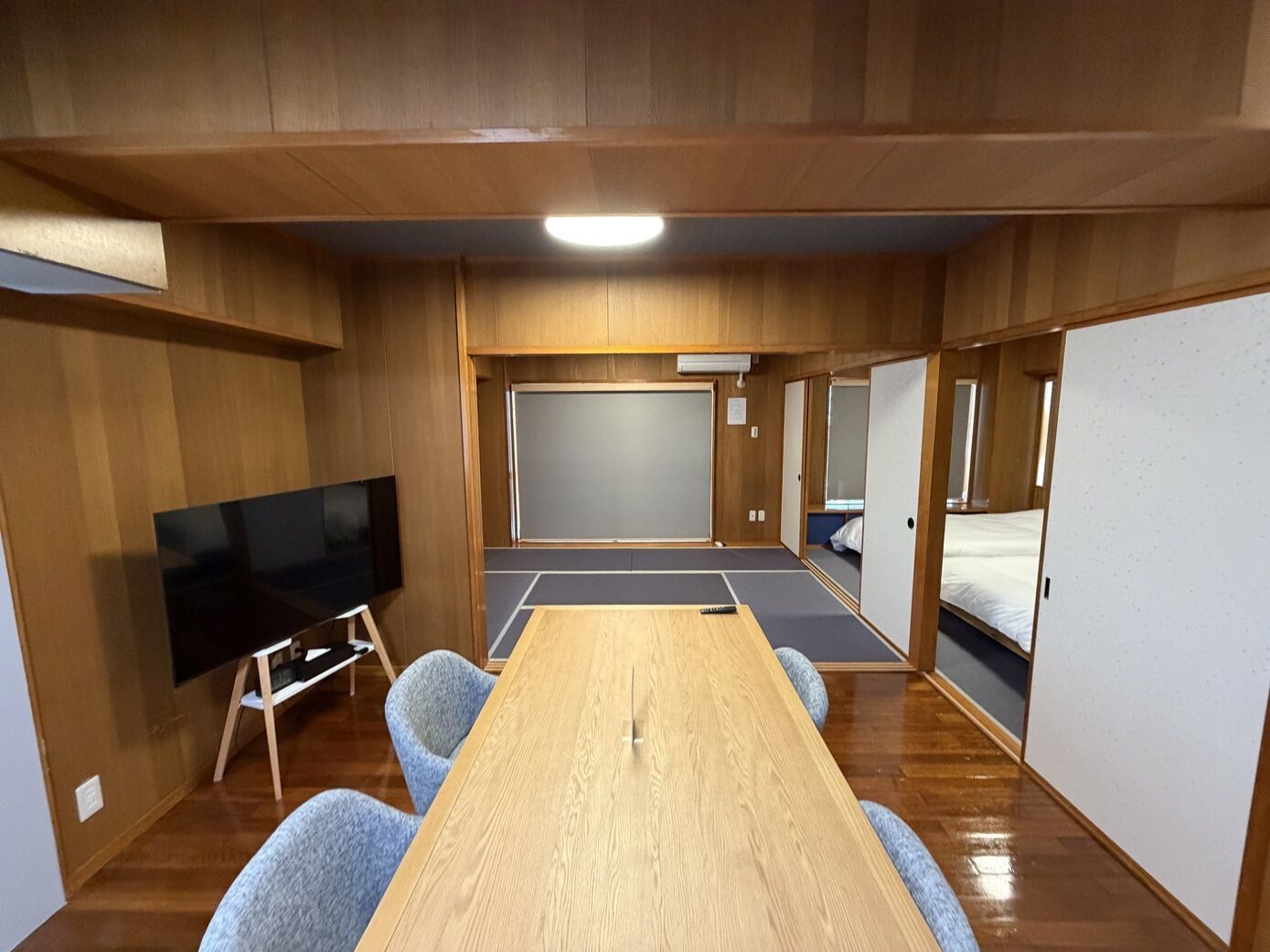 Une pièce avec une longue table en bois, un téléviseur à écran plat et un futon servant de lit.