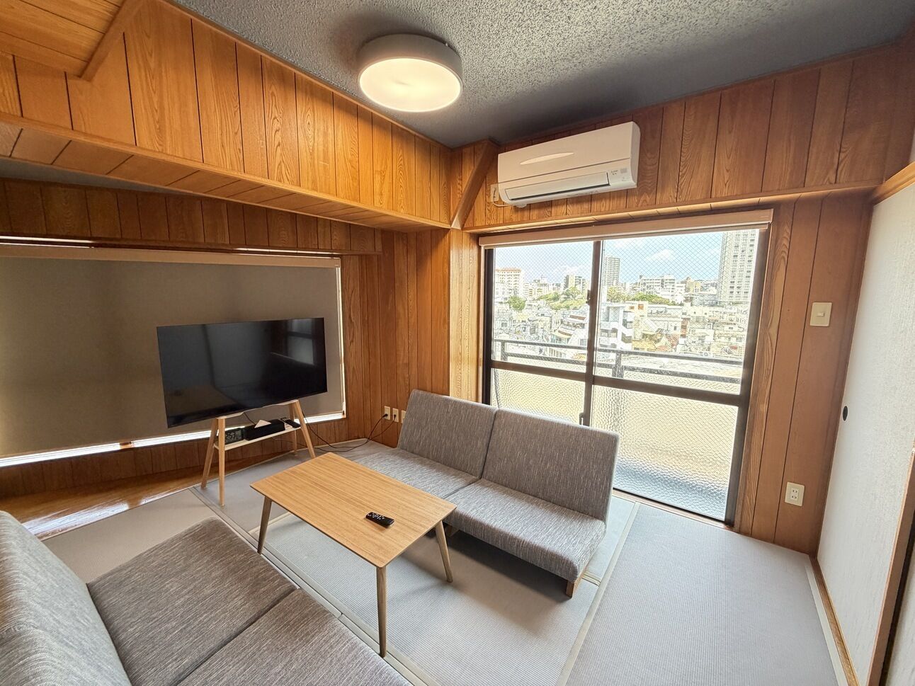 Une pièce avec un intérieur en bois, un canapé, un téléviseur et une fenêtre donnant sur la ville.