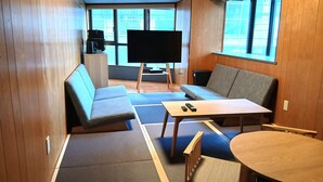 A modern room with a large TV, a sofa, a small table, and a round table. - Kokusai Towns Inn (Naha)