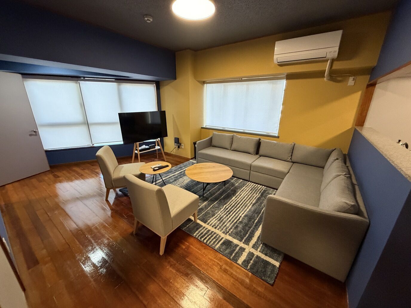 Un salon comprenant un canapé, des fauteuils, une table basse, un téléviseur posé sur un meuble et une grande fenêtre.