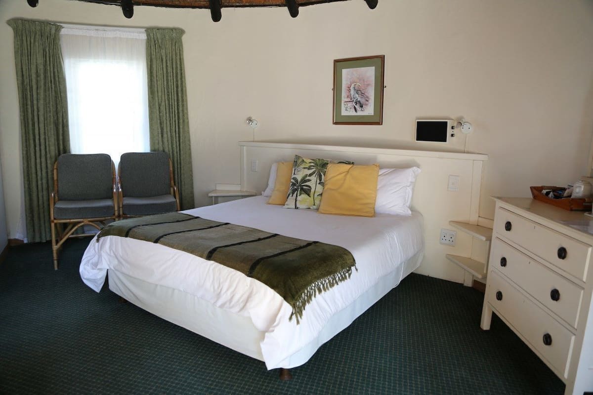 A hotel room with a large bed, two chairs, a bedside table, a lamp, and a picture on the wall.