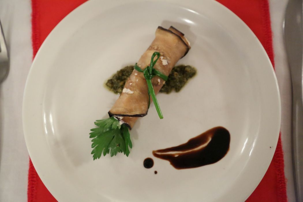 Une assiette blanche contenant un aliment enroulé, une garniture verte et une sauce, le tout posé sur une nappe rouge.