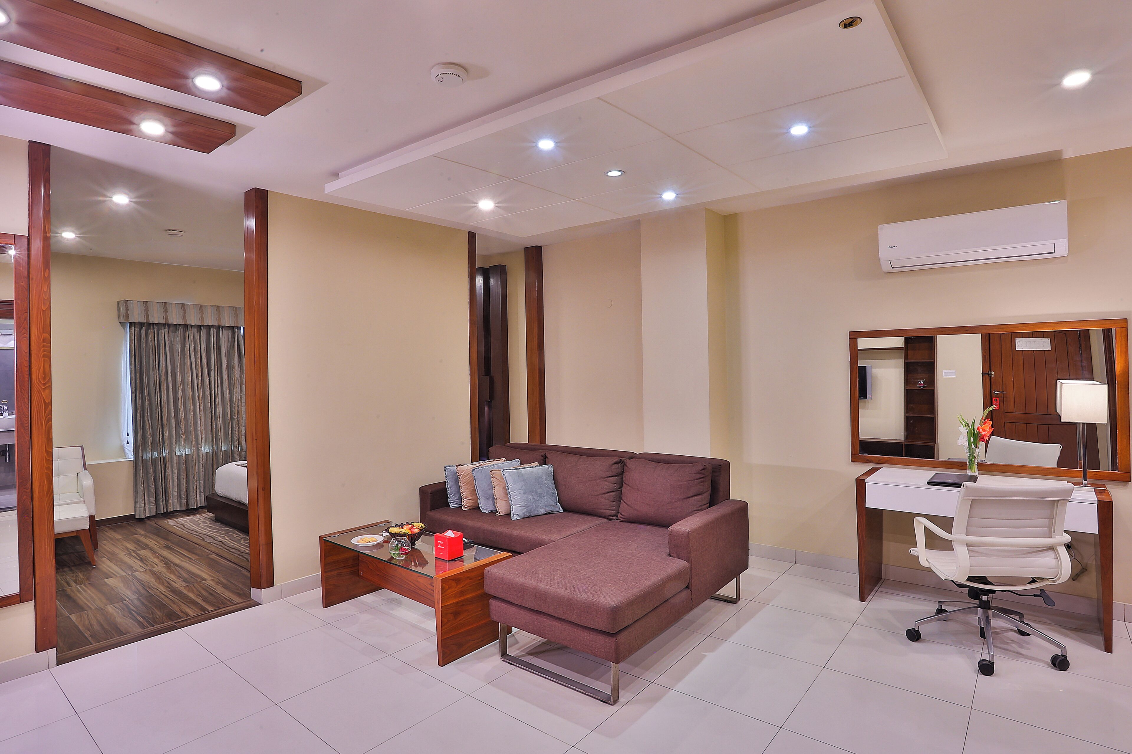 Una habitación de hotel moderna con un sofá modular, un escritorio, una silla y un espejo grande.