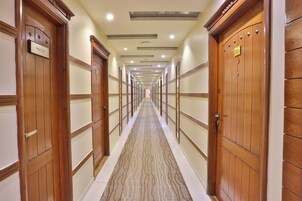 Un pasillo de hotel con puertas de madera, alfombra estampada e iluminación empotrada en el techo.
