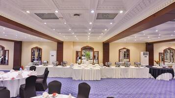A banquet hall with round tables, black chairs, and a patterned carpet.