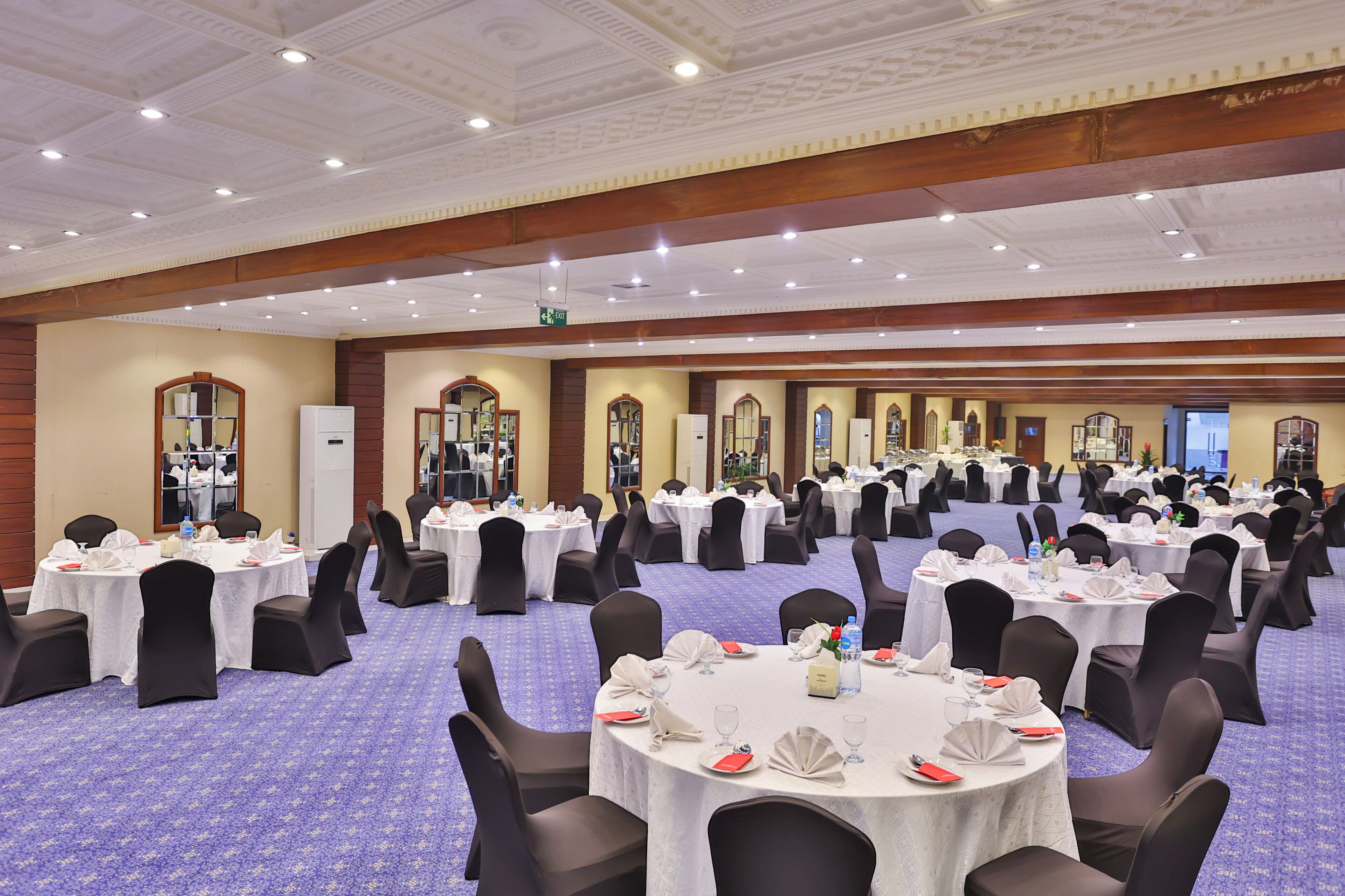 A banquet hall with round tables, black chairs, and white tablecloths.