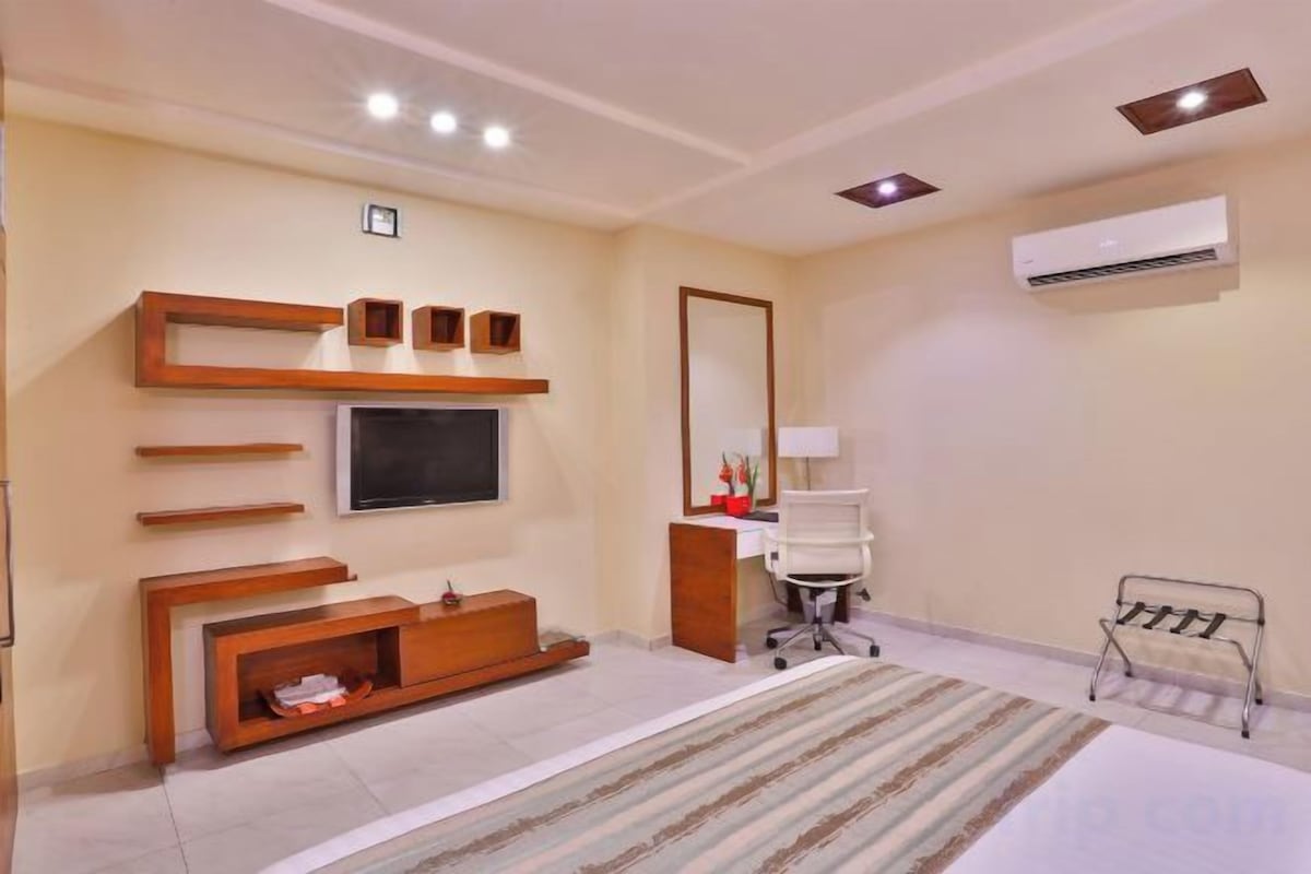 A hotel room with a bed, a TV mounted on the wall, a desk, and a chair.