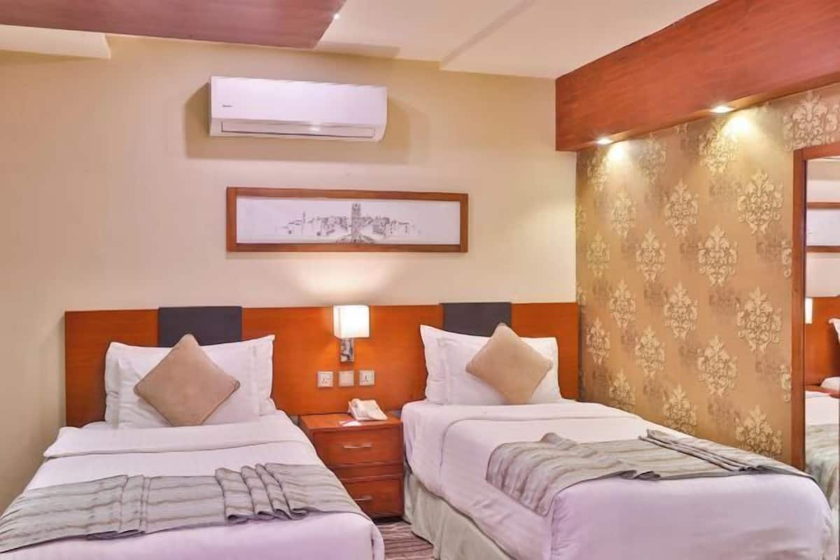 A hotel room with two beds, a nightstand, an air conditioning unit, a framed picture on the wall, and a patterned wallpaper.