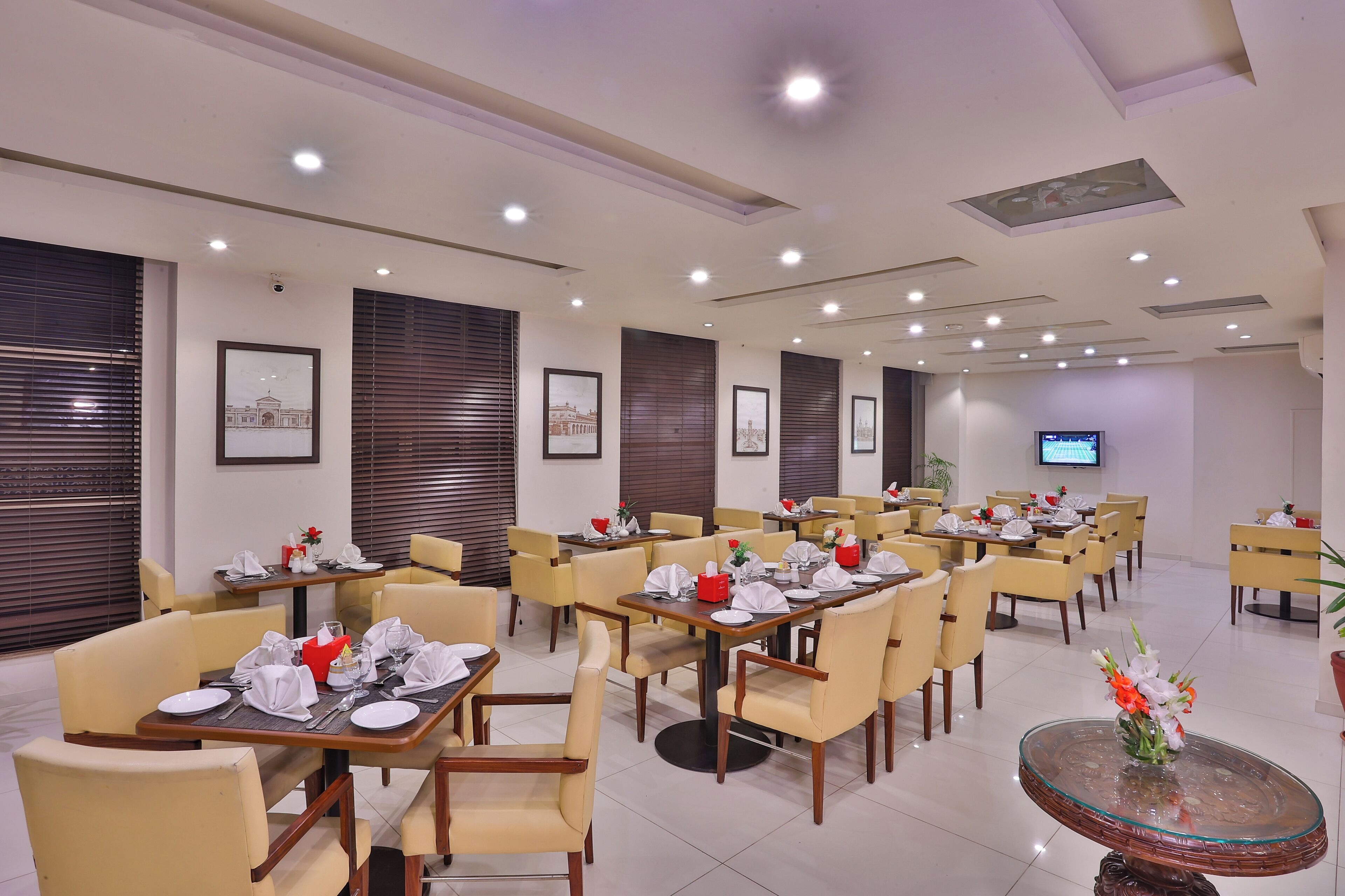 A hotel dining area with multiple tables, chairs, and a television screen.