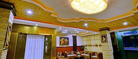 A lobby with a chandelier, sofas, a reception desk, and a wall with a painting.