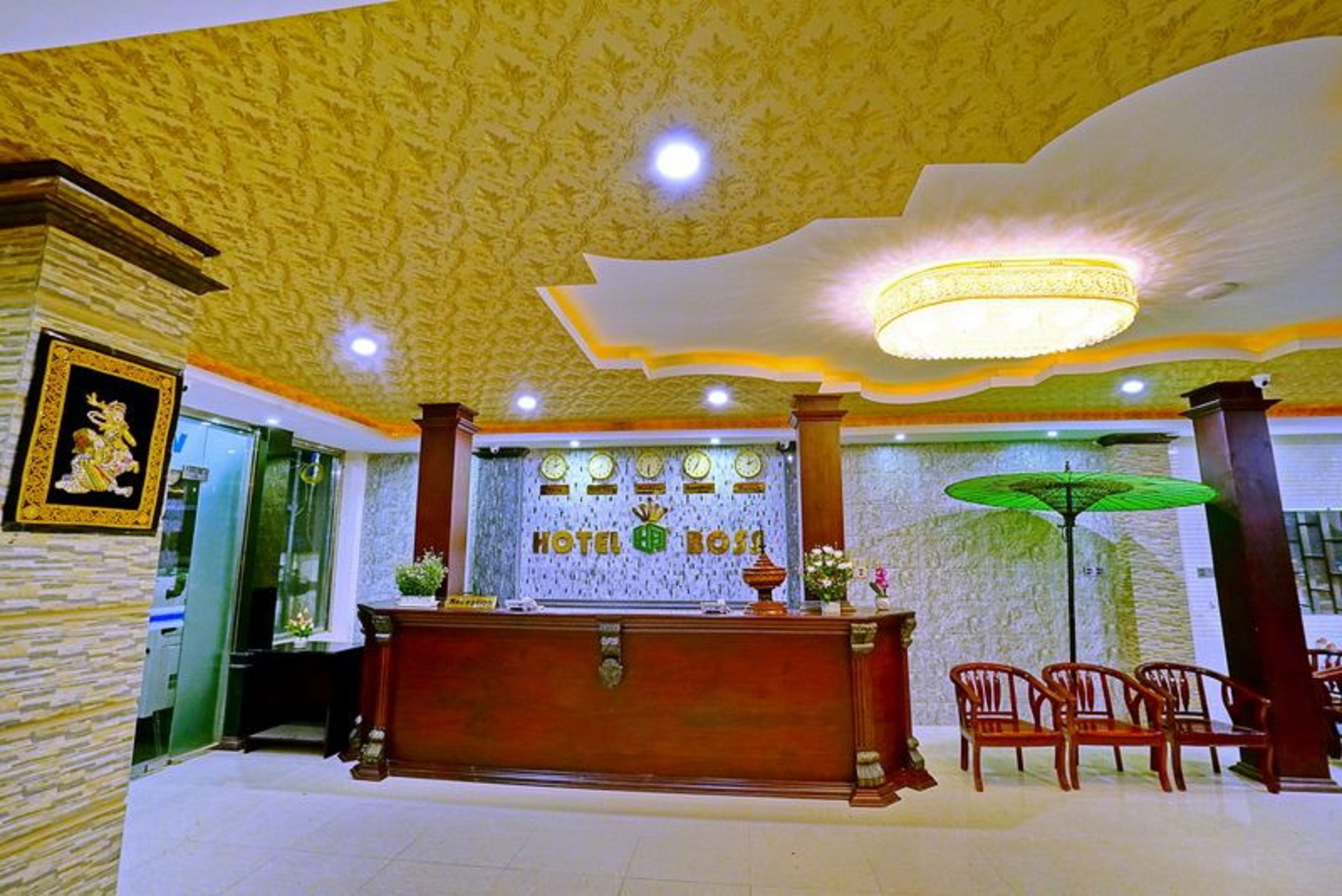 A hotel reception area with a wooden reception desk, a chandelier, and a green umbrella.