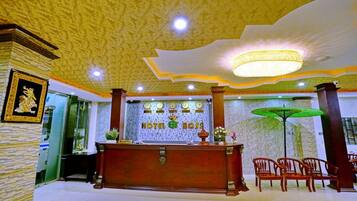 A hotel reception area with a wooden reception desk, a chandelier, and a green umbrella.