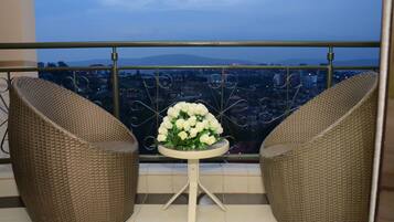 Ein Balkon mit Korbstühlen und einem Tisch mit einer weißen Blumenkomposition, mit Blick auf eine Stadtlandschaft.