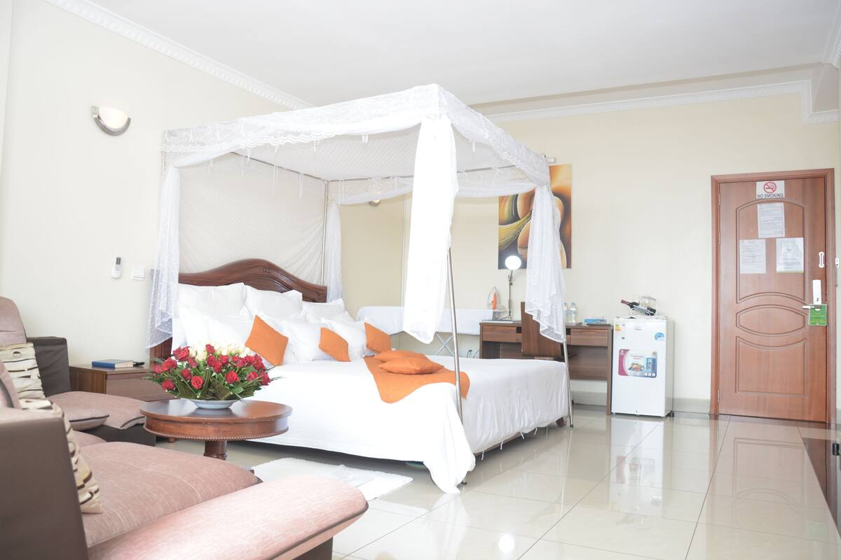 Habitación de hotel con cama con dosel, mesita de noche, refrigerador pequeño y una silla.