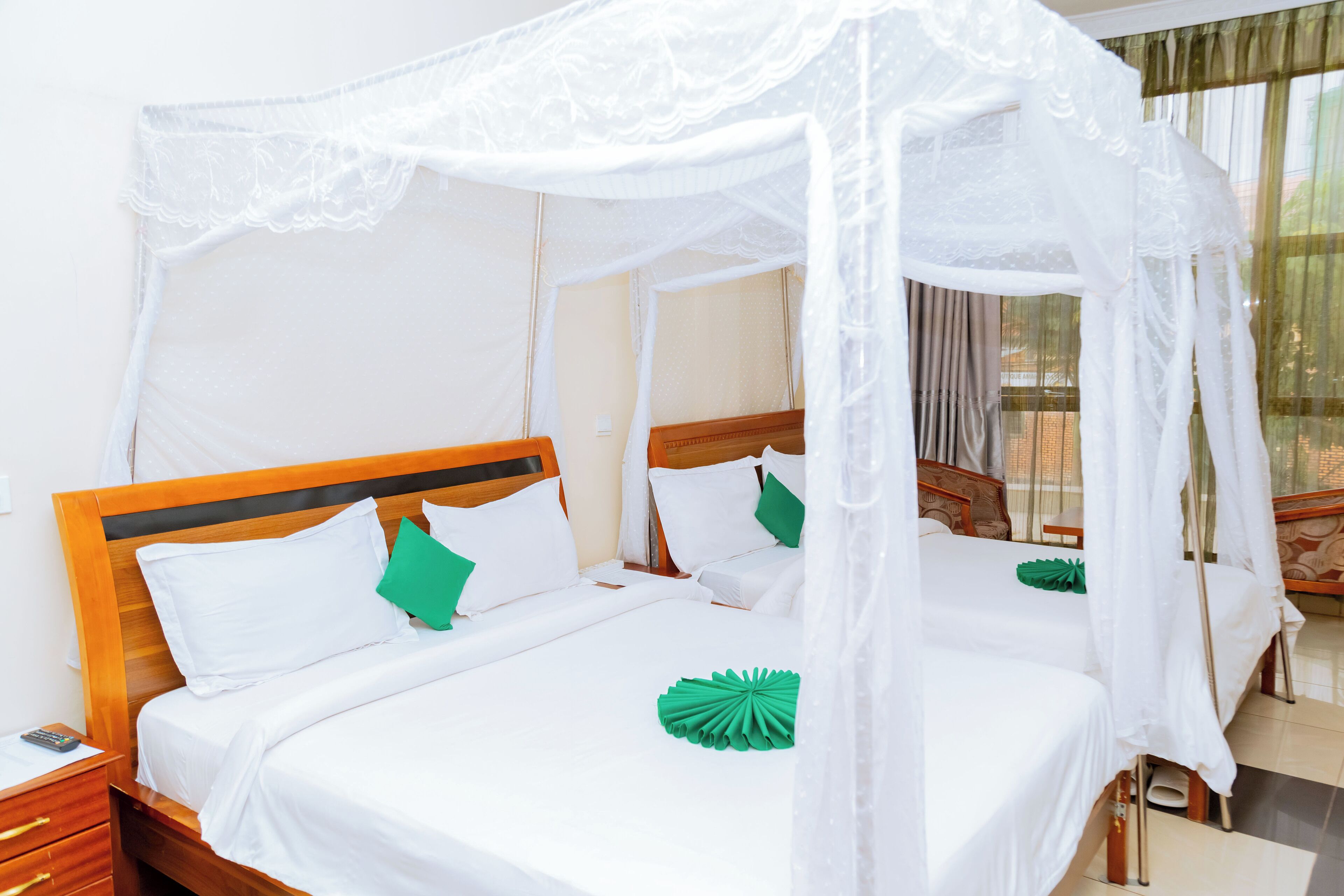 A four-bed room with a canopy bed, wooden headboard, white bedding, and green decorative pillows.