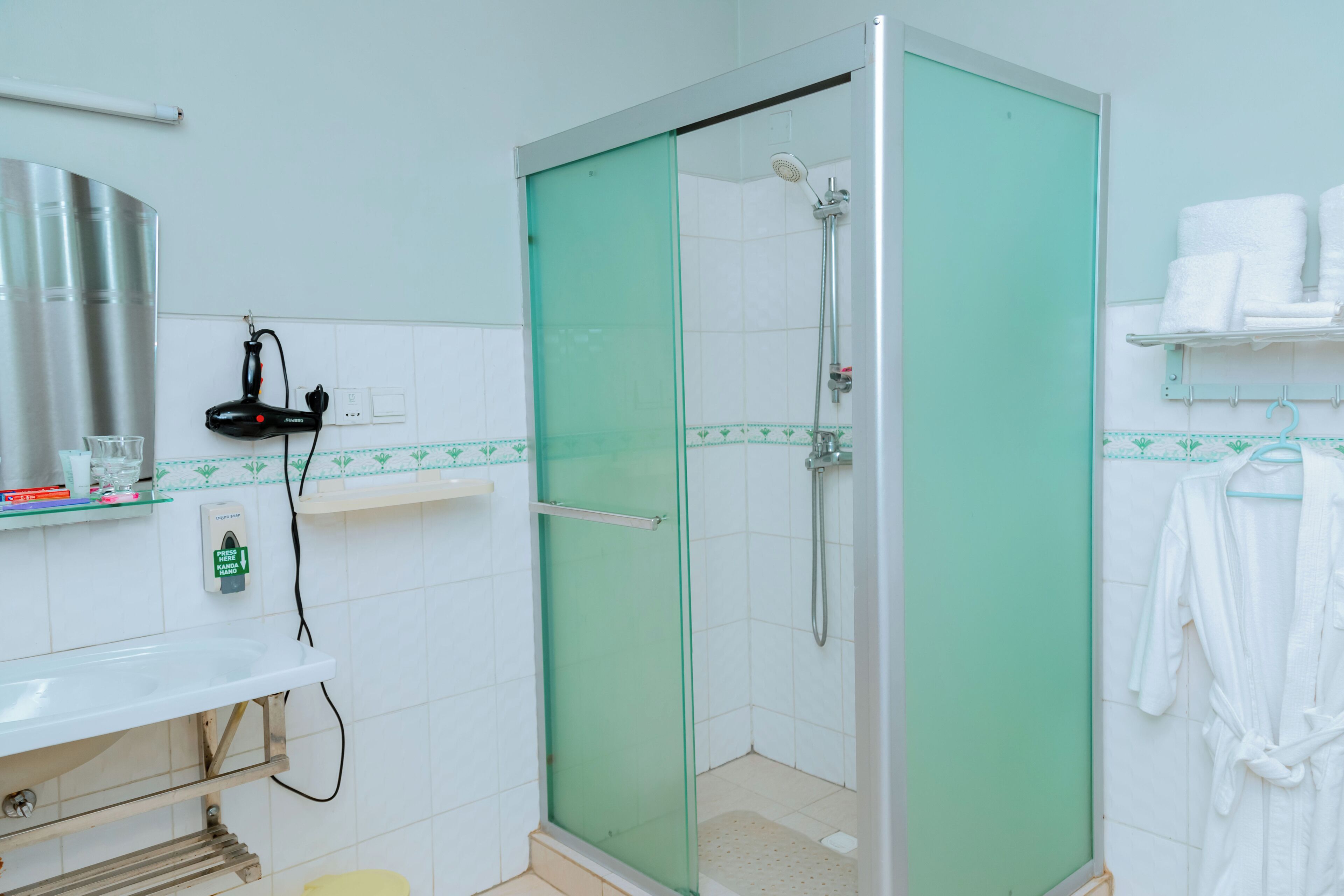 A modern bathroom with a glass-enclosed shower, white tiles, a sink with a mirror, and a towel rack with white towels.