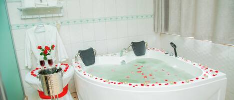 A bathroom with a large bathtub, a shower, and a toilet. There are towels and a vase with flowers on the counter.
