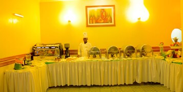 A buffet setup with a chef, a coffee machine, and a painting on the wall.