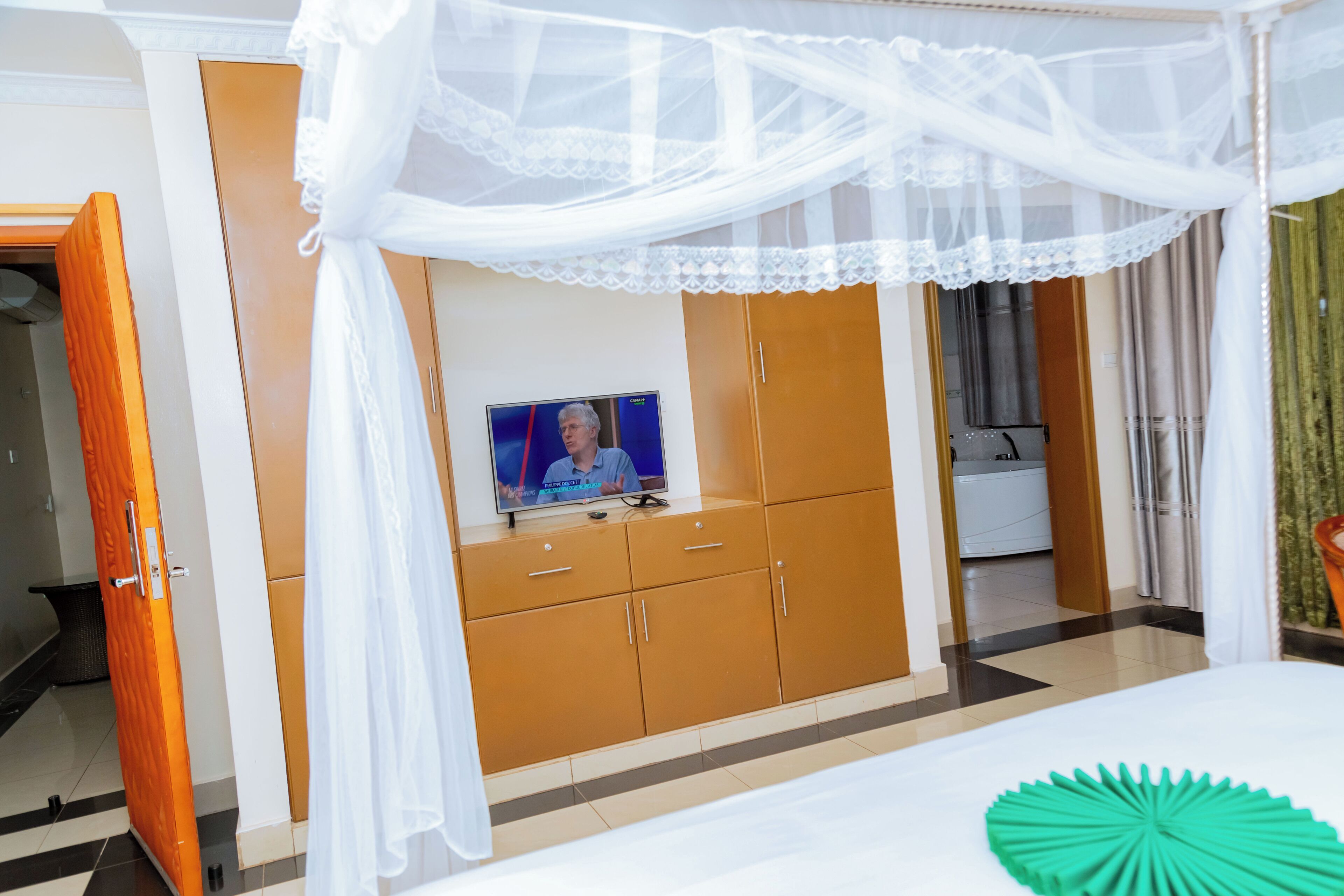 A bedroom with a bed, a television on a wooden cabinet, and a bathroom visible through an open door.