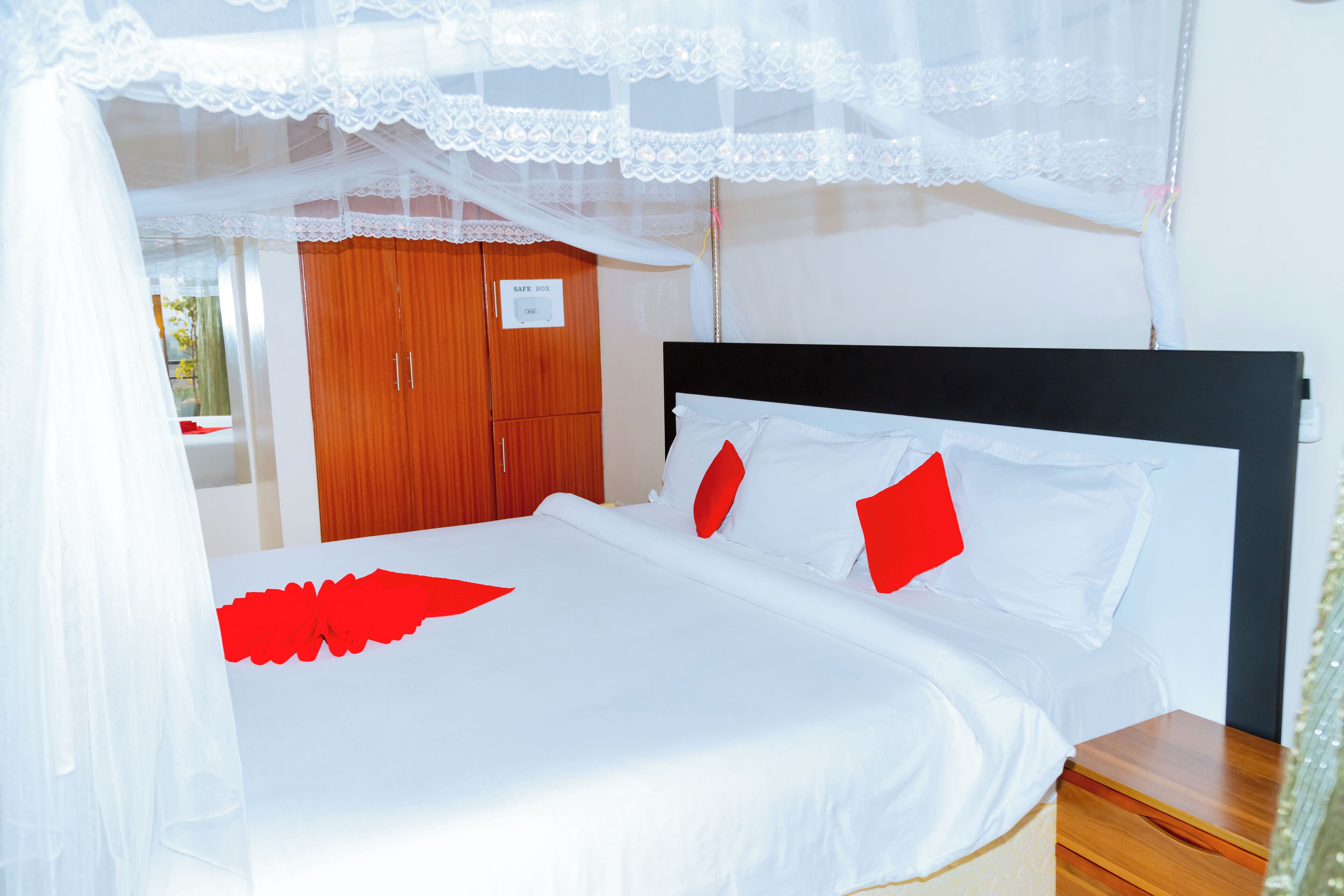 A neatly made bed with white and red bedding, a wooden wardrobe, and a sign indicating a safe box.