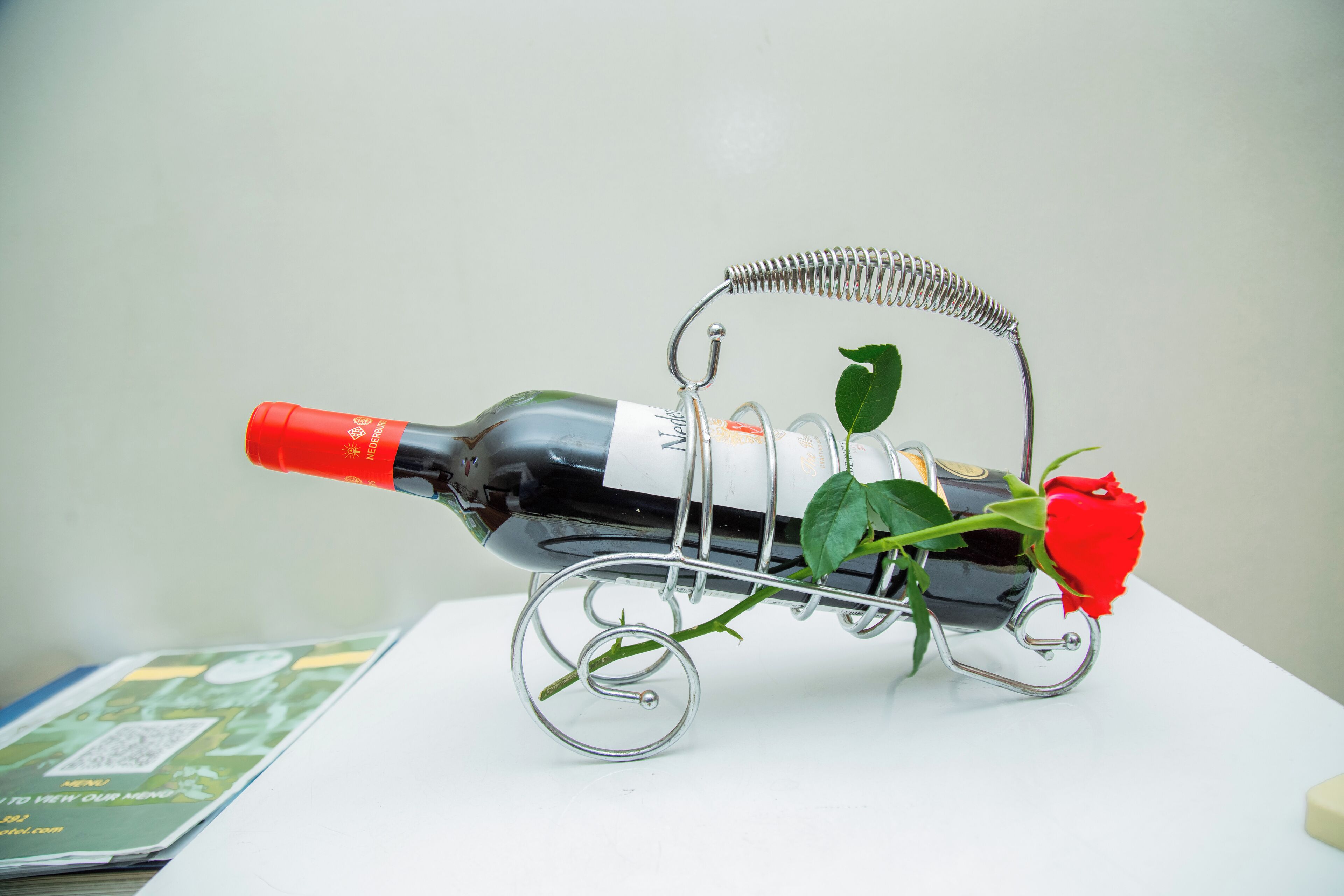 A wine bottle with a rose and leaves on a metal stand.