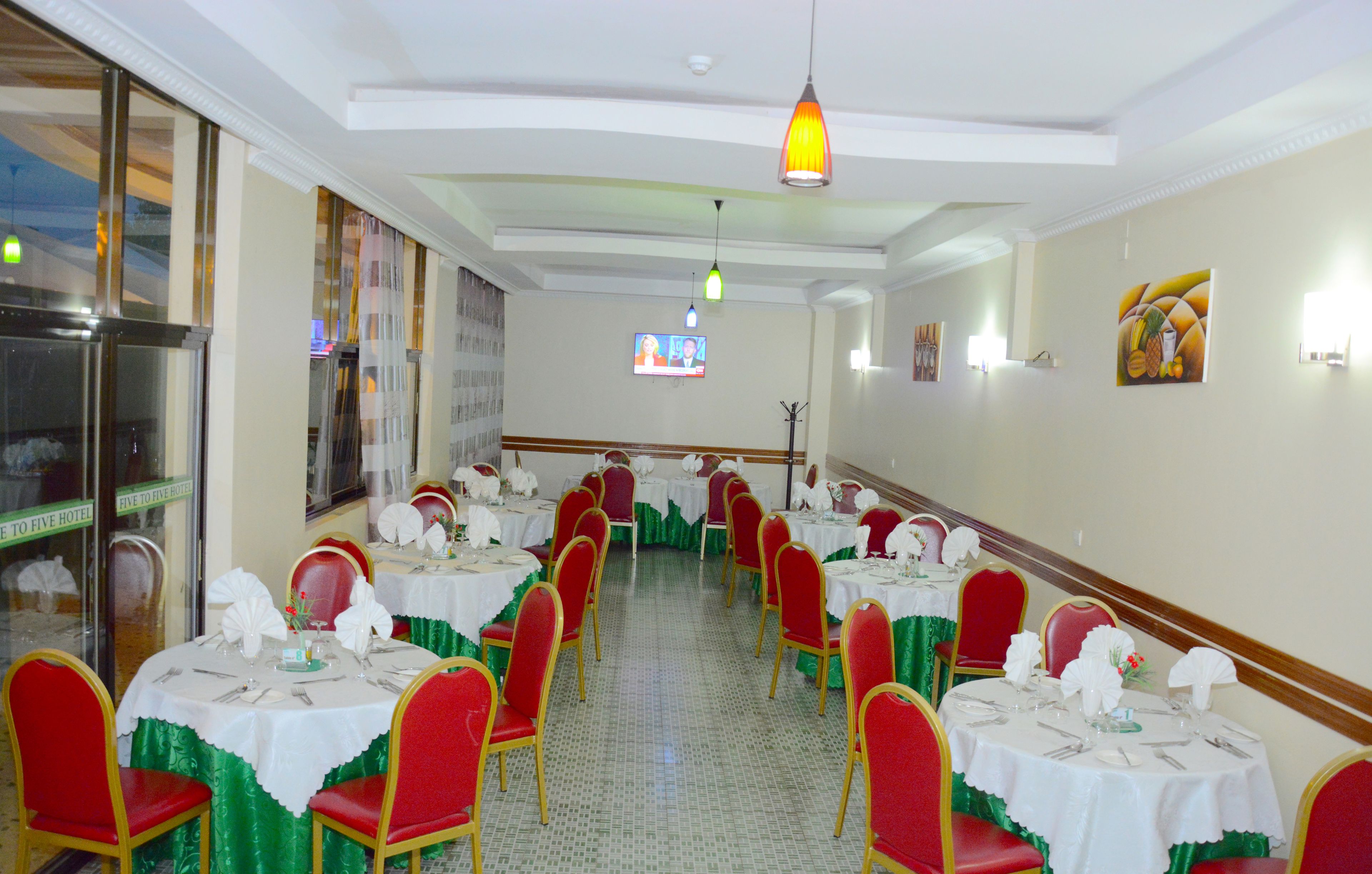 A banquet hall with round tables set for dining, red chairs, and a large window on the left.