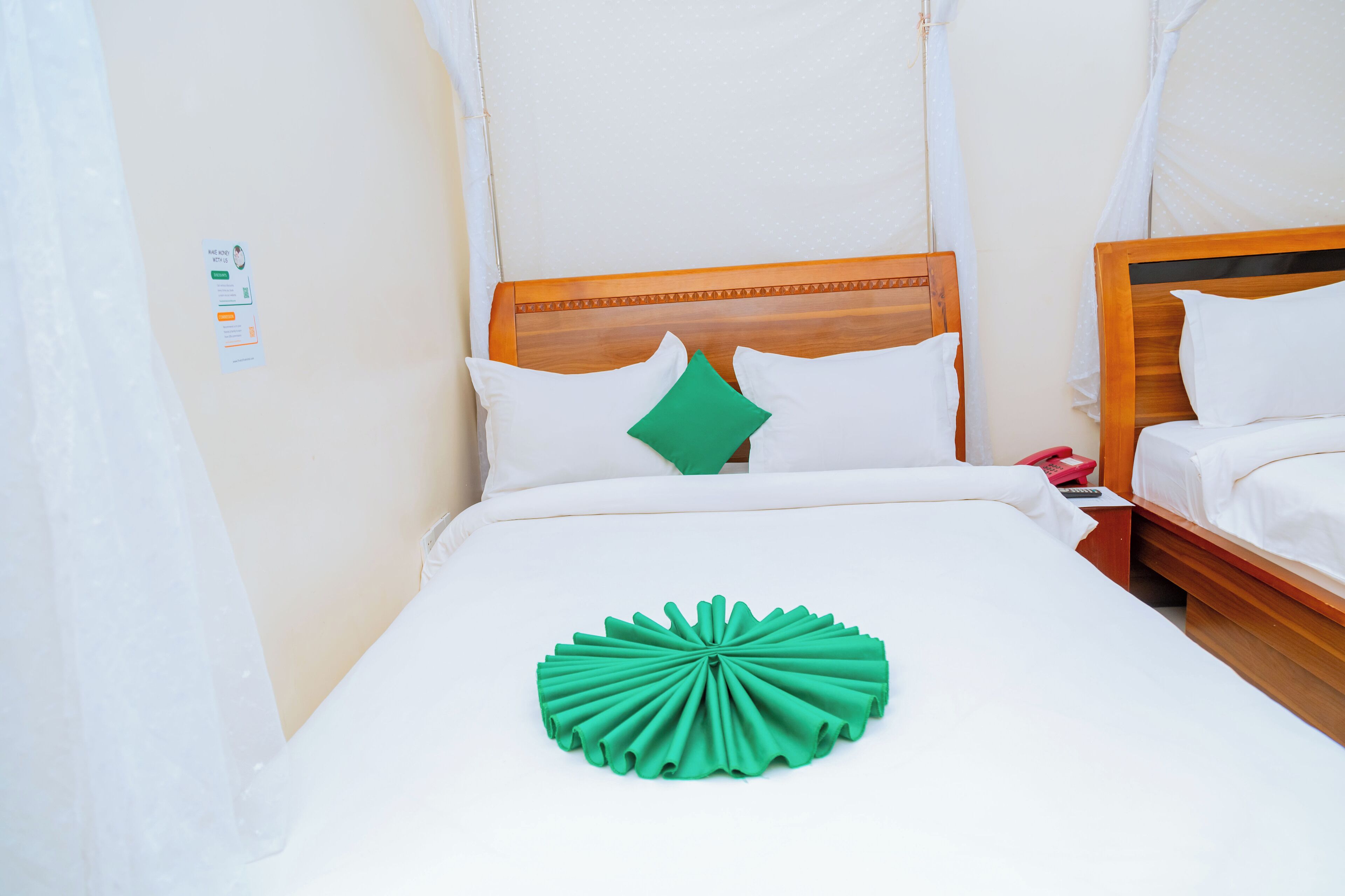 A neatly made bed with white linens, a green decorative pillow, and a wooden headboard.