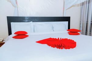Una cama bien hecha con sábanas blancas y almohadas rojas, un cabecero negro y un dosel blanco.