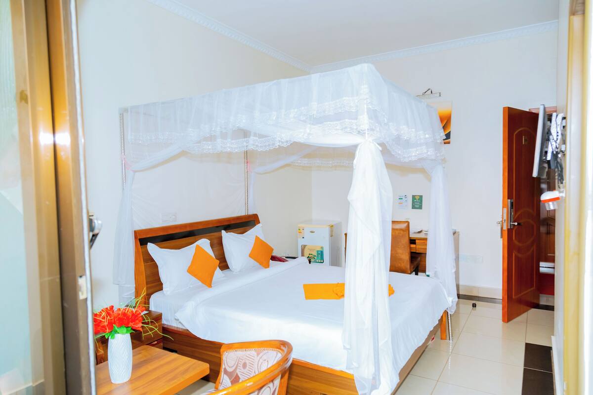 Habitación de hotel con una cama, una mesita de noche con un florero, una silla de madera y un armario.