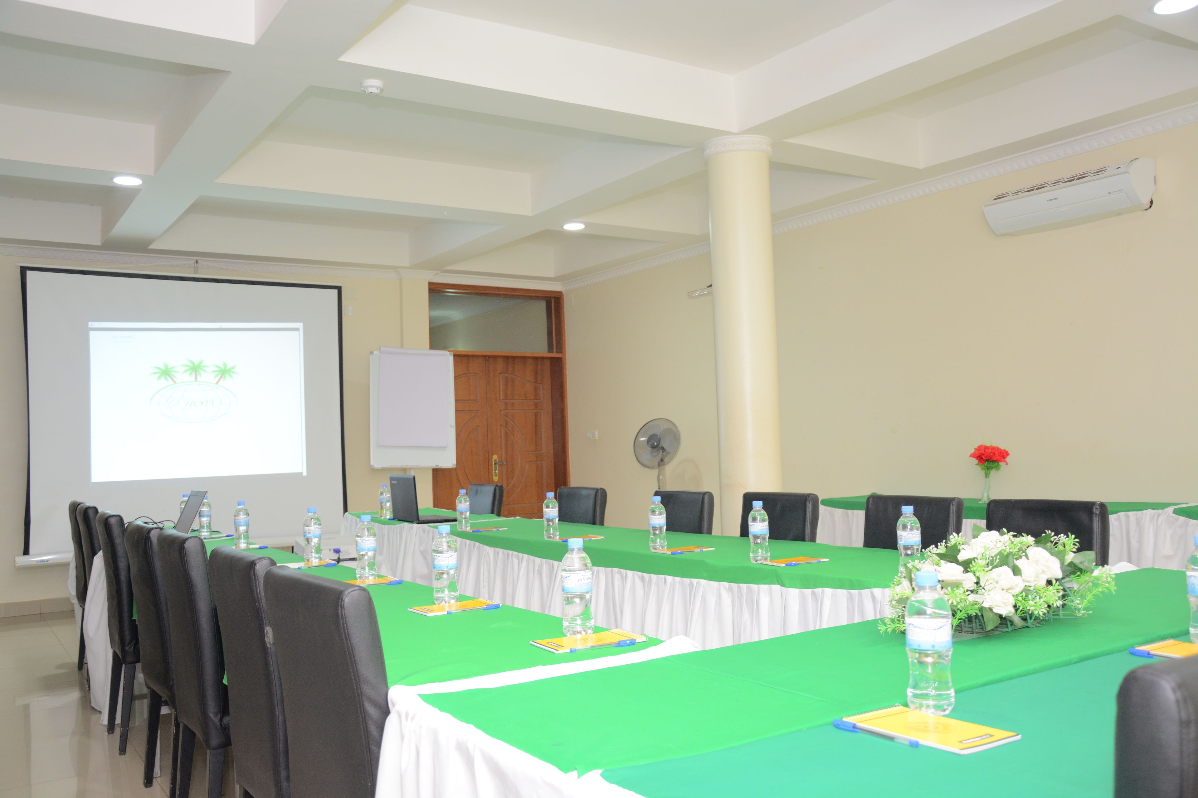A conference room with a long table, chairs, a projector screen, and an air conditioning unit.