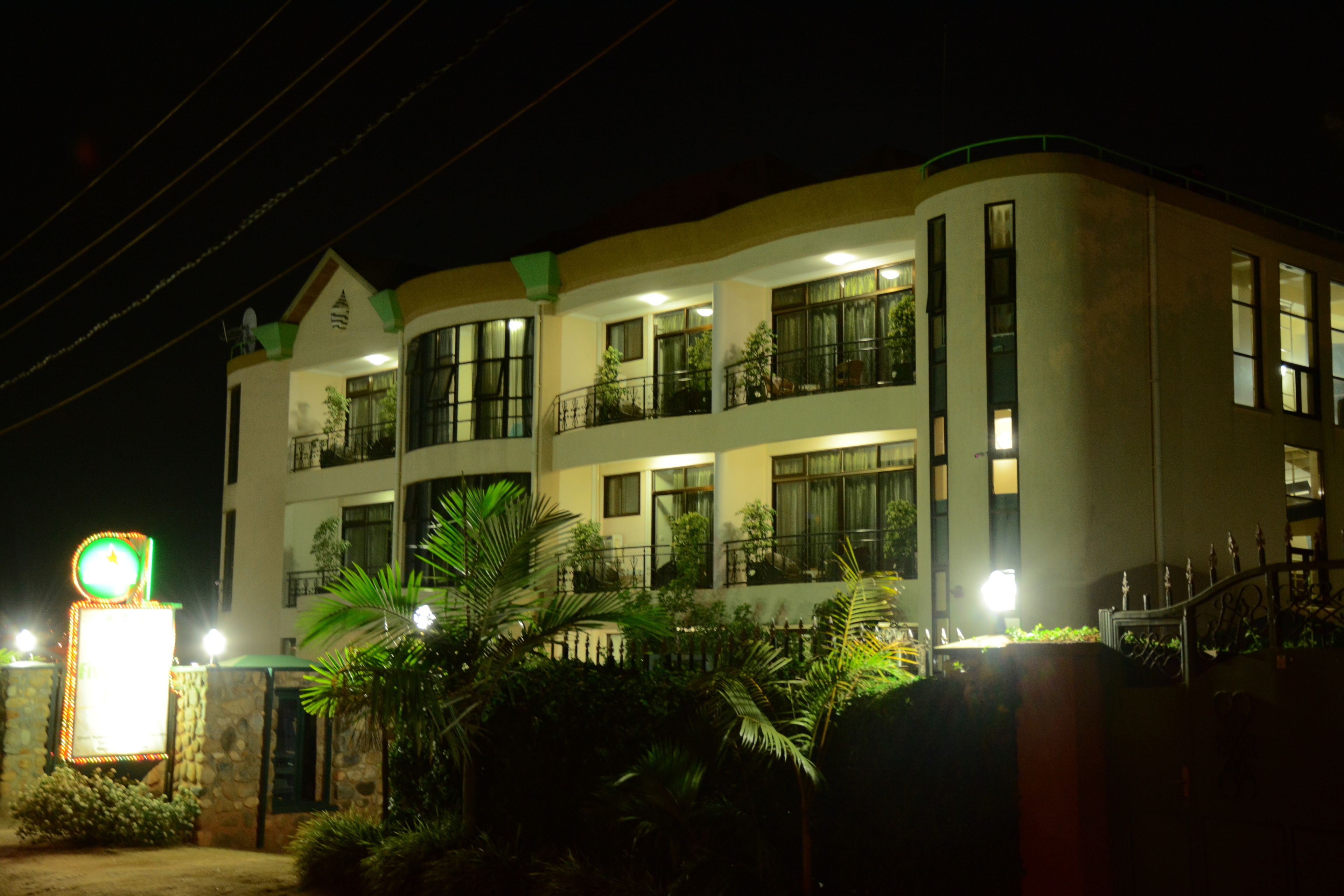 A multi-story hotel with balconies, a well-lit entrance, and a signboard.