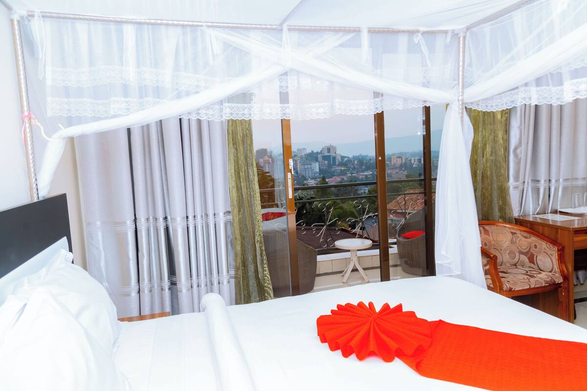 Habitación de hotel con cama, balcón y vistas a la ciudad, además de una mesa con sillas.