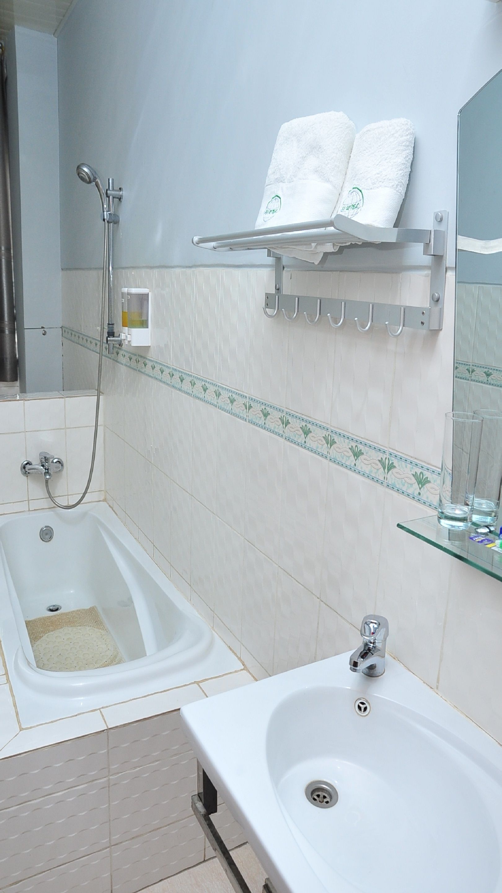 Un baño con bañera, lavamanos, toallero con toallas, cabezal de ducha y espejo.