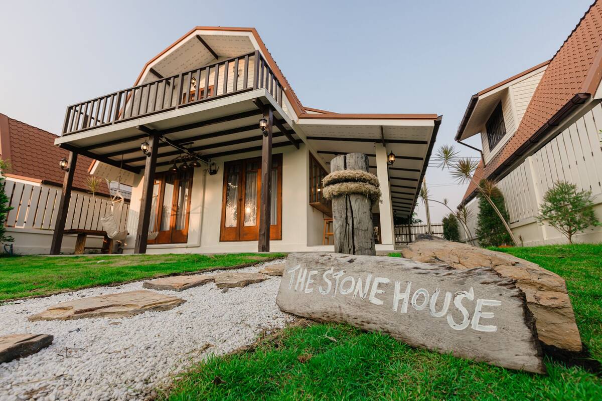 A house with a stone facade, a balcony, and a sign reading "THE STONE HOUSE".