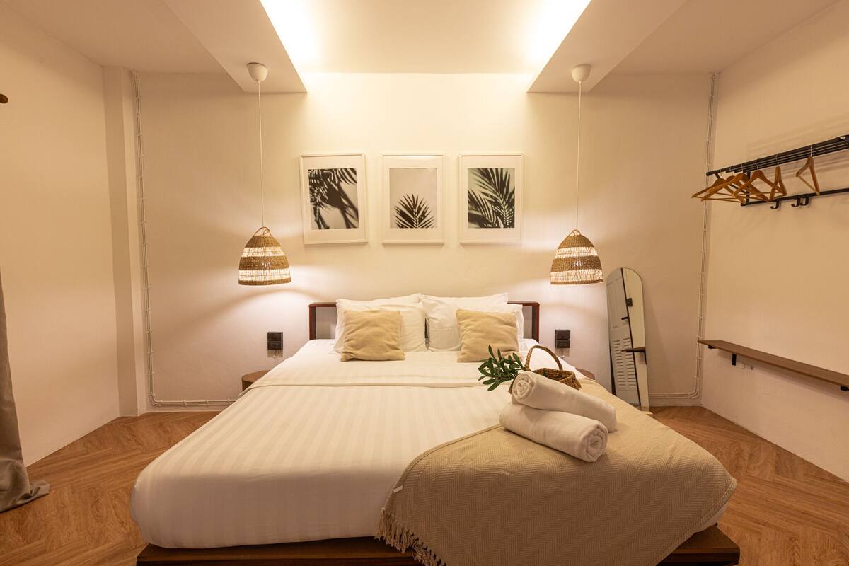 A neatly arranged bedroom with a large bed, two bedside lamps, and three framed leaf artworks on the wall.