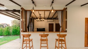A modern kitchen with a large window, three wooden bar stools, and pendant lighting. - 60s Town (Hua Hin)