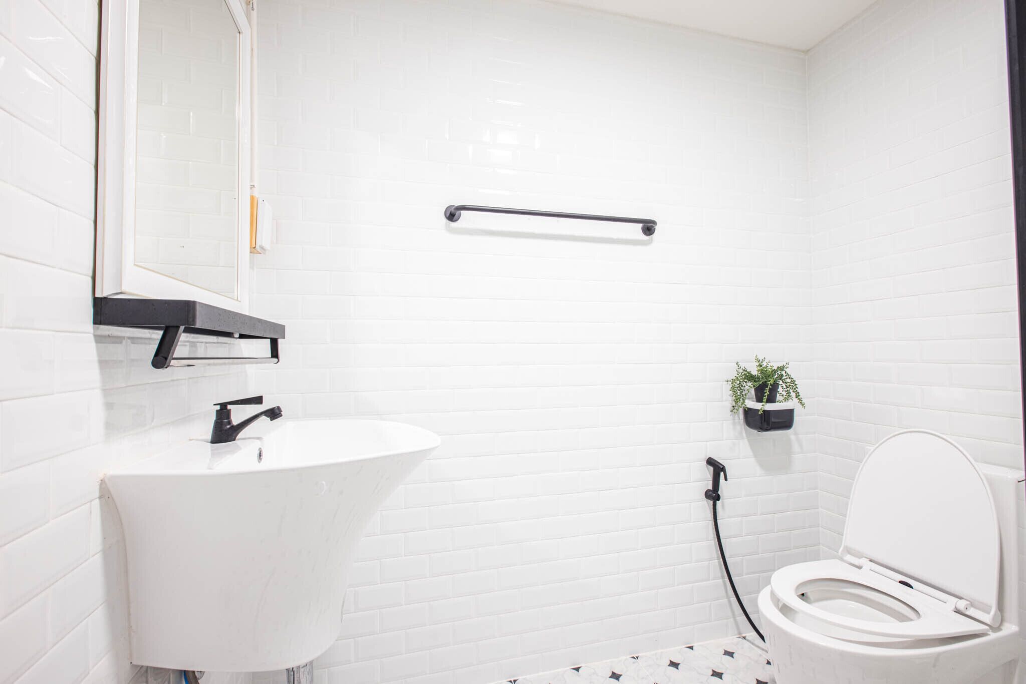 A bathroom with a white sink, a black towel rack, a white toilet, and a small potted plant on the wall.