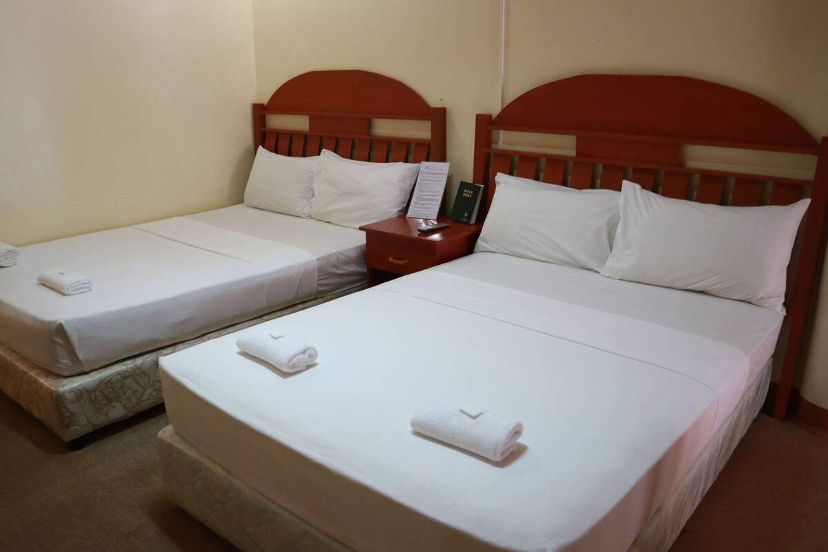 Two single beds with white linens and towels, a wooden headboard, and a nightstand with a book and a remote control.