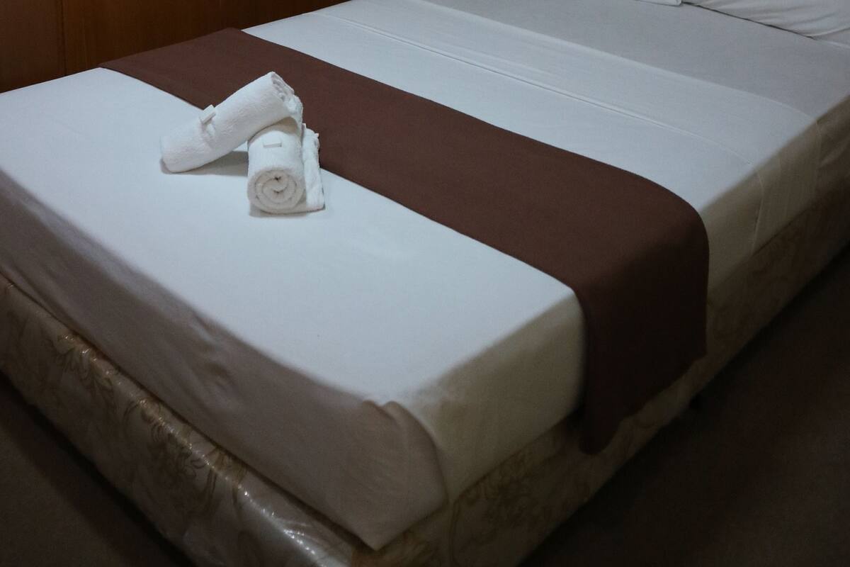 A hotel room with a bed, a wooden wardrobe, and a wall-mounted light fixture.