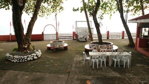 An outdoor seating area with tables and chairs, surrounded by trees and a view of the water. - Coral Dive Resort (Catarman)