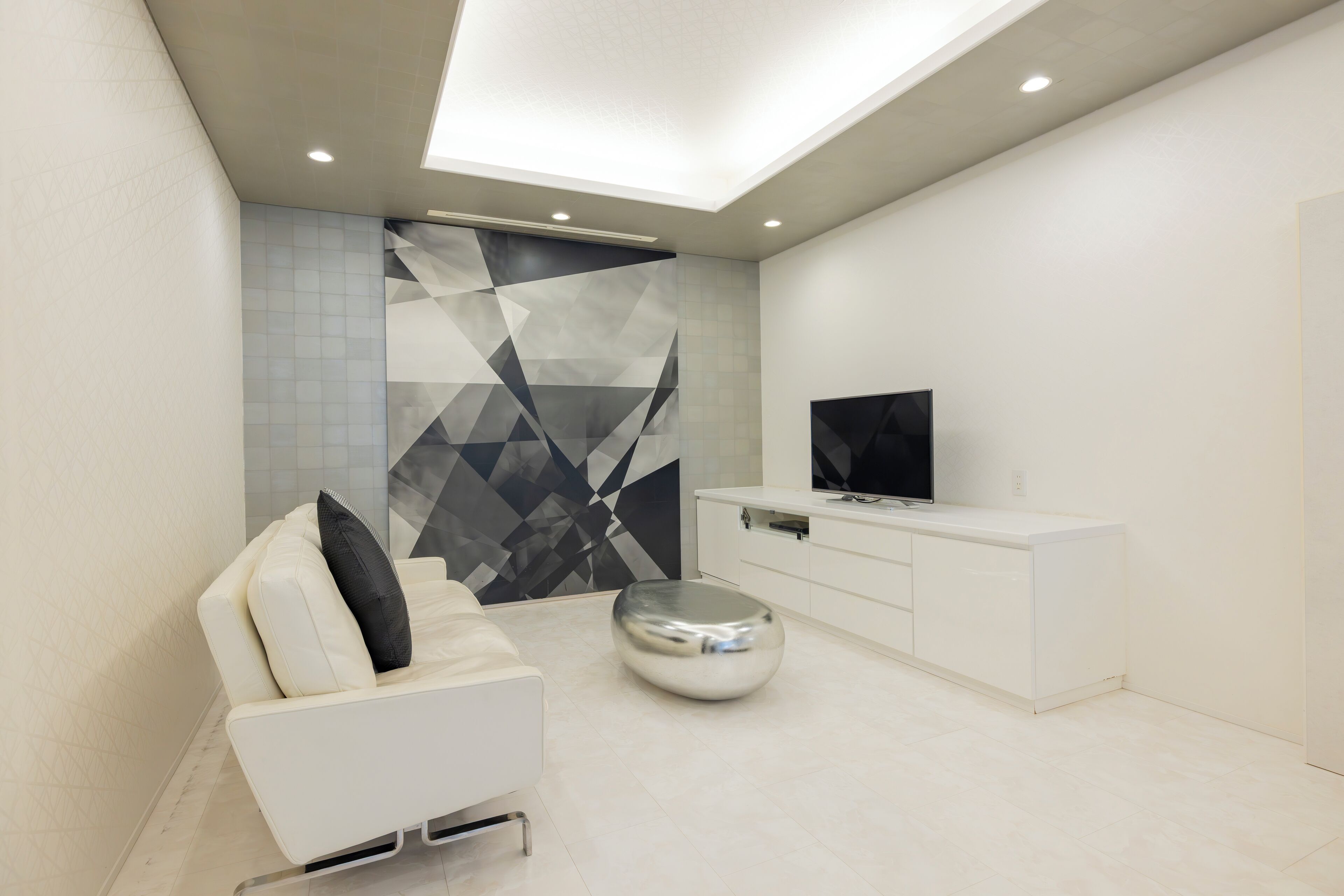 A modern living room with a white sofa, a round ottoman, a flat-screen TV, and a white cabinet.