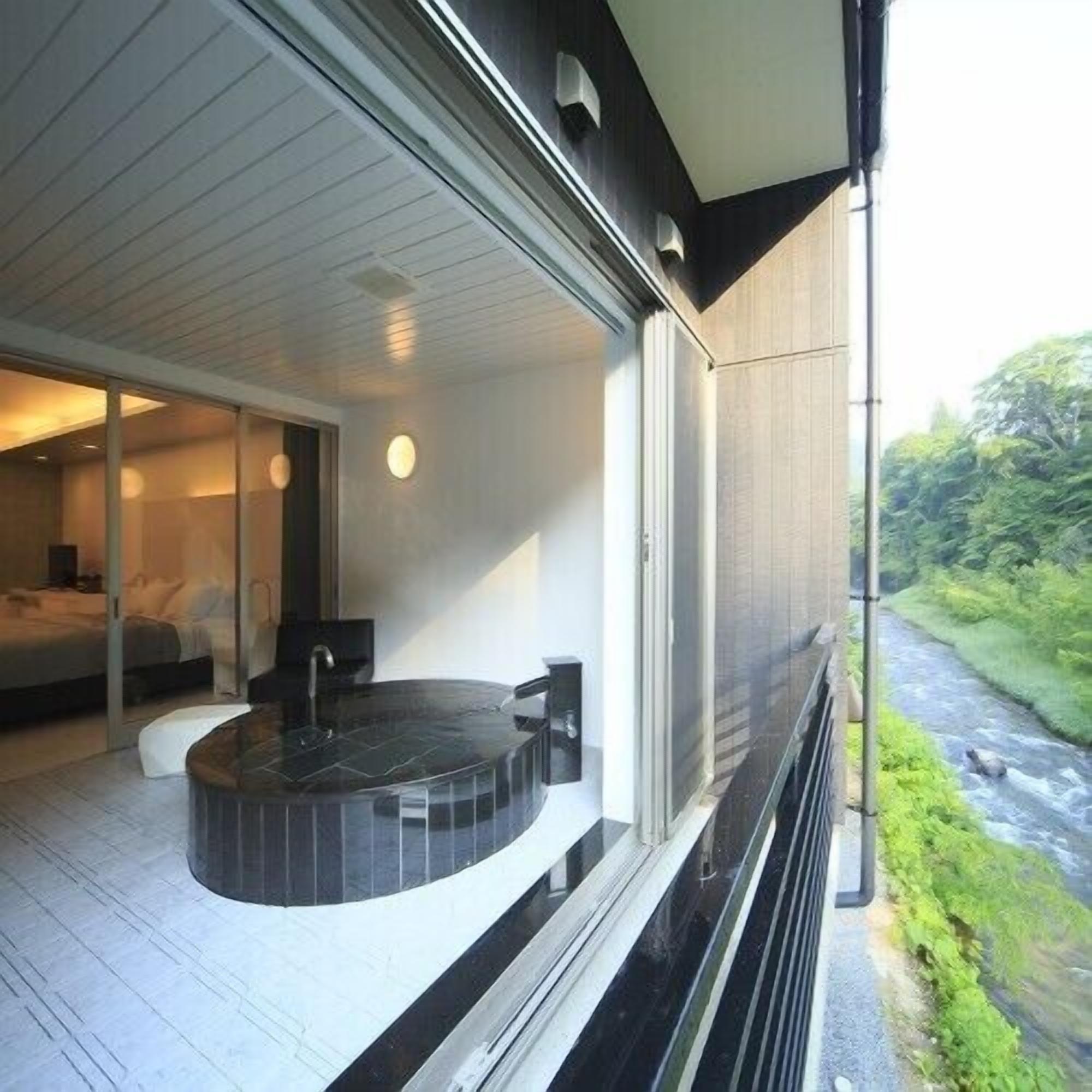 Ein modernes Hotelzimmer mit einer runden Whirlwanne, einem großen Fenster mit Flussblick und einem separaten Schlafzimmer mit Bett und Nachttisch.