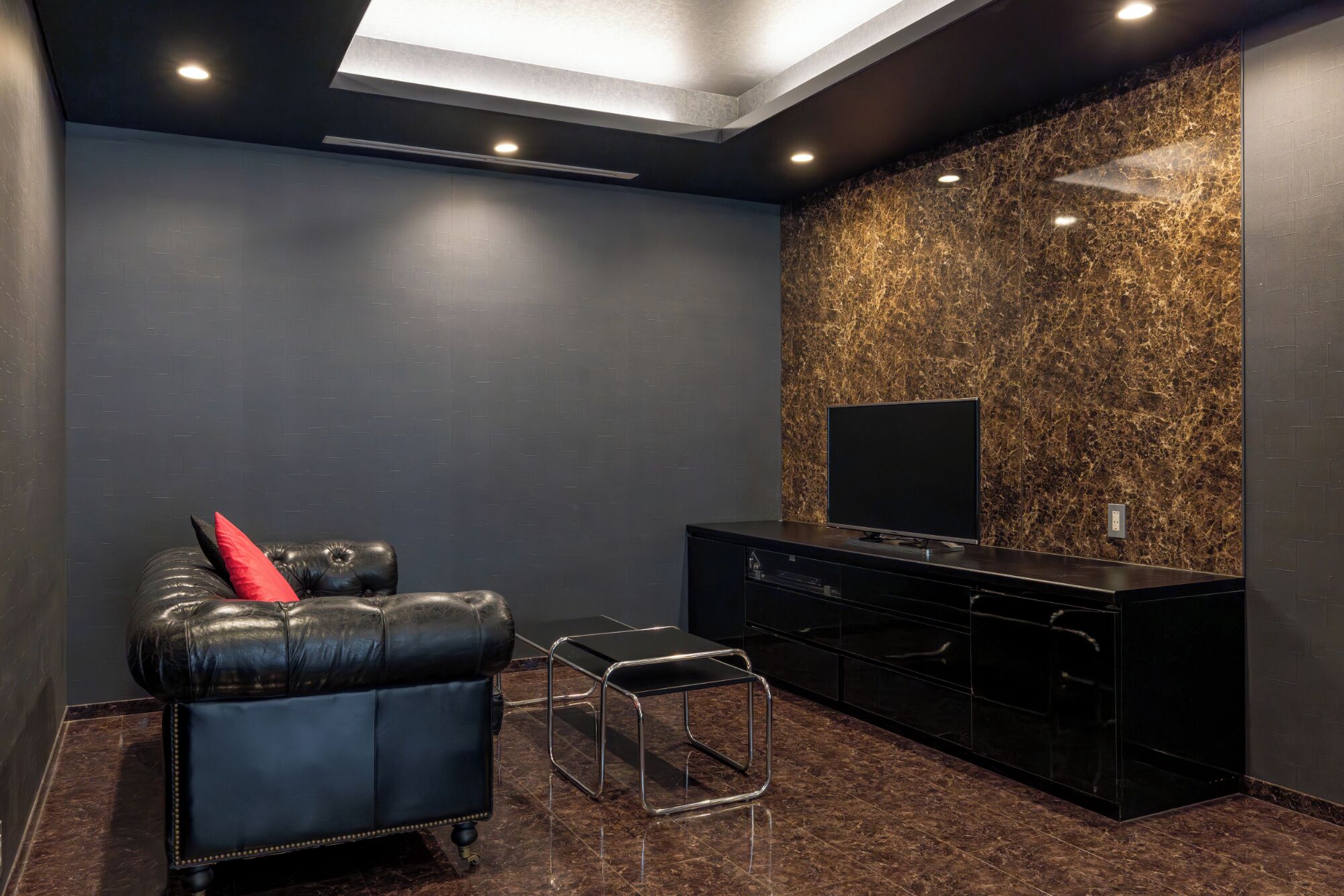 Una sala de cine en casa moderna con un sofá de cuero, una mesita y un televisor sobre un mueble negro.