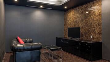 Una sala de cine en casa moderna con un sofá de cuero, una mesita y un televisor sobre un mueble negro.