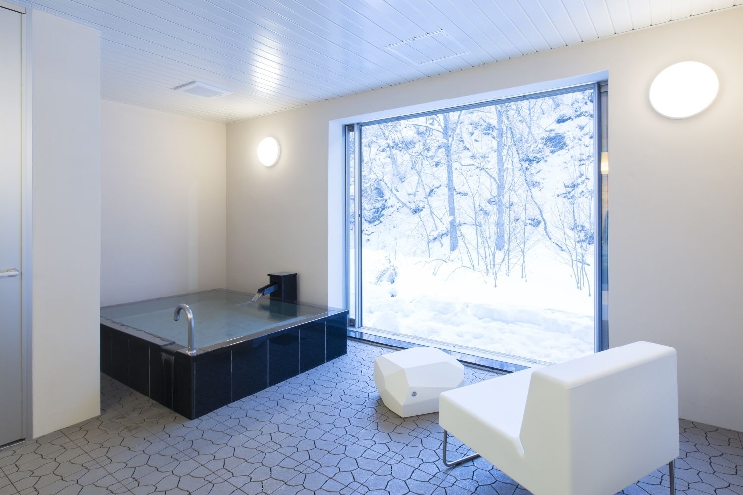 A modern bathroom with a large window, a bathtub, and a white chair.