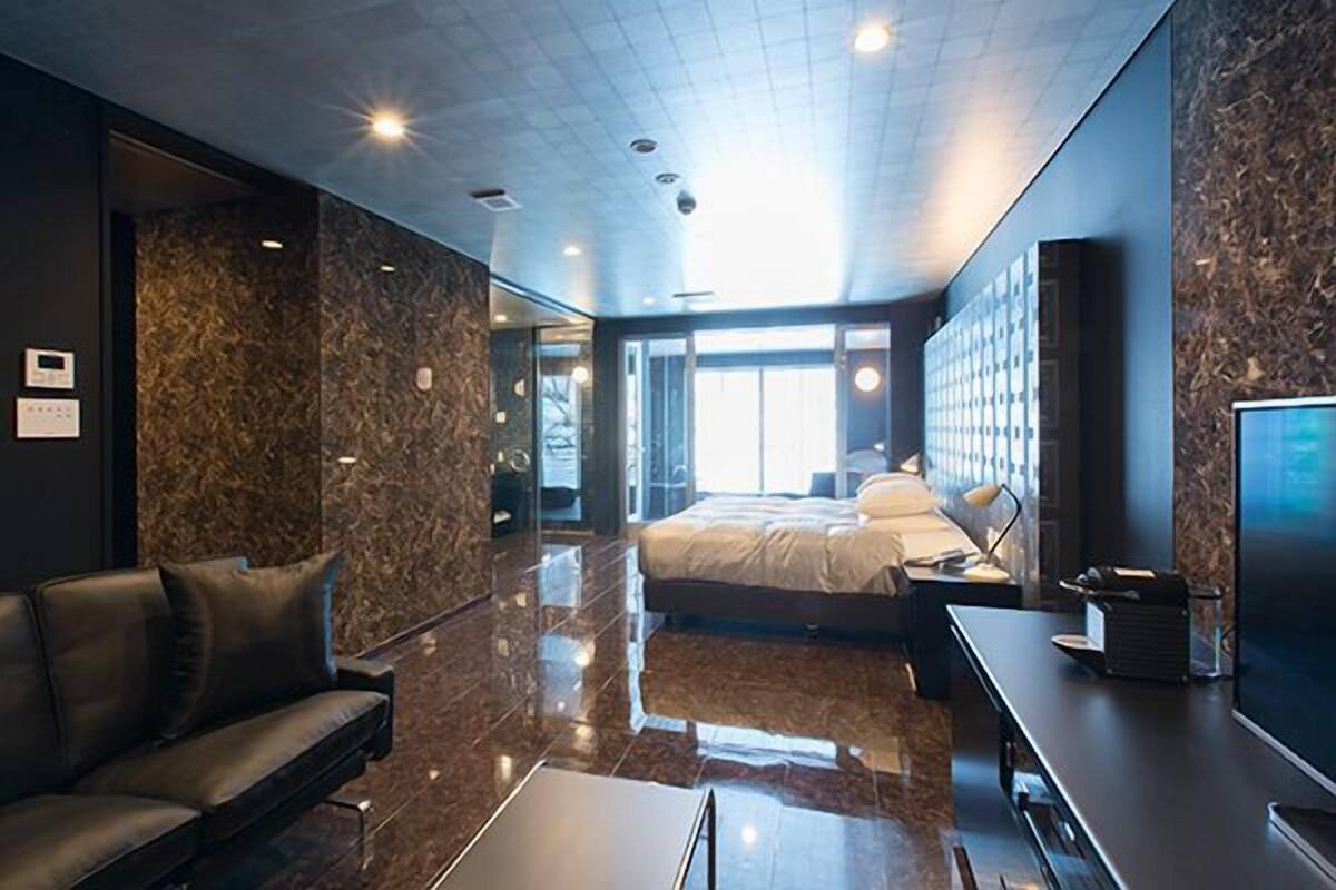 A modern hotel room with a large bed, a sofa, a flat-screen TV, and a marble-textured wall.