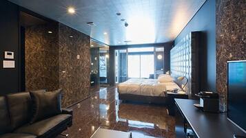 A modern hotel room with a large bed, a sofa, a flat-screen TV, and a marble-textured wall.