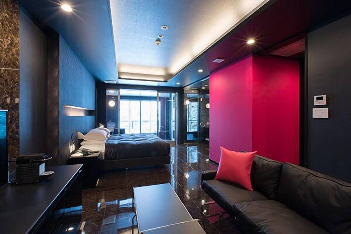 A modern hotel room with a bed, a sofa, a desk, and a large window.