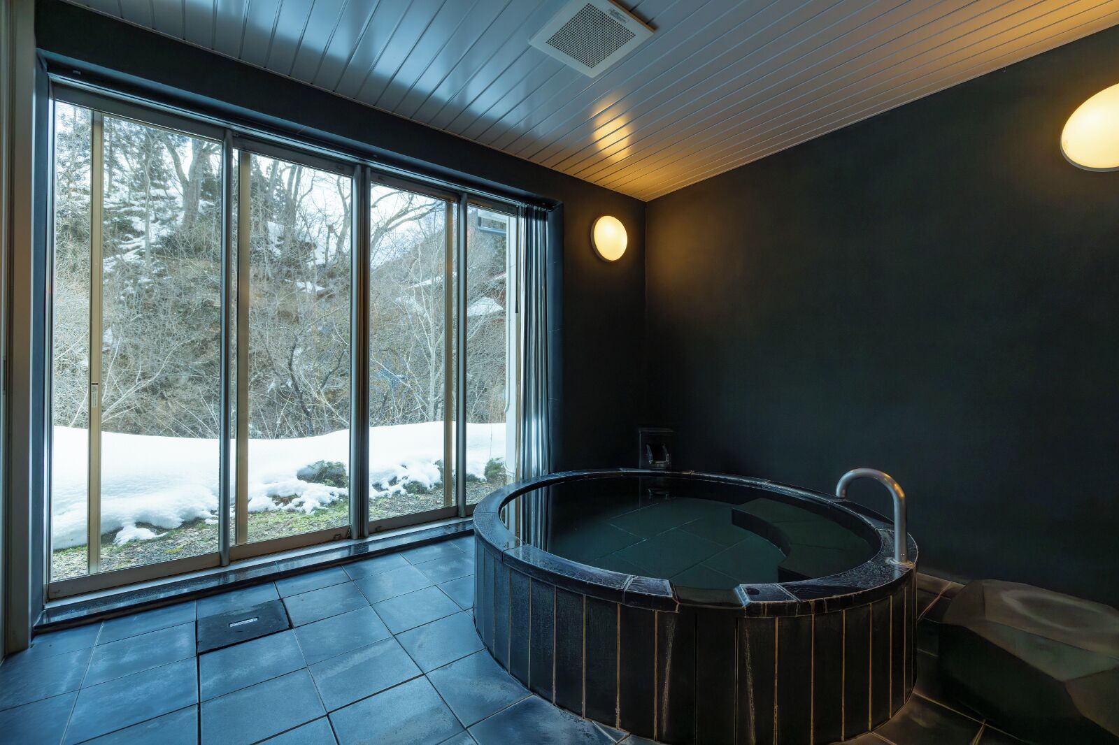 Una stanza spa con un'ampia finestra, una vasca idromassaggio e una parete scura.