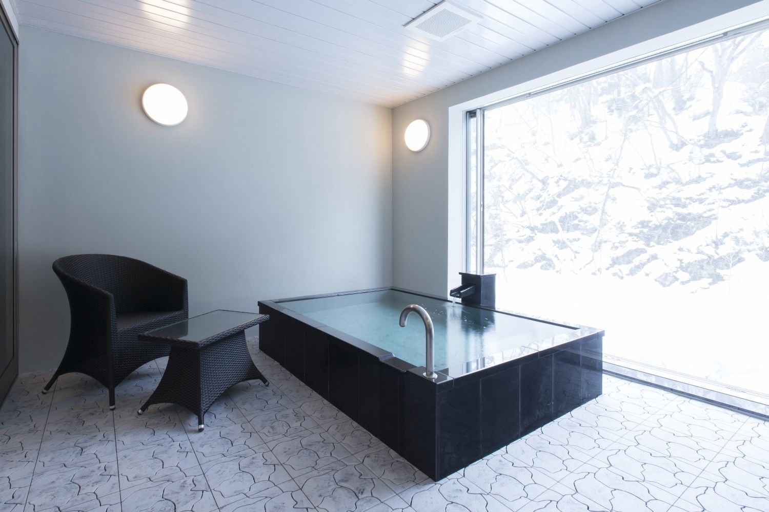 A modern bathroom with a glass-enclosed bathtub, a black chair, and a small table.